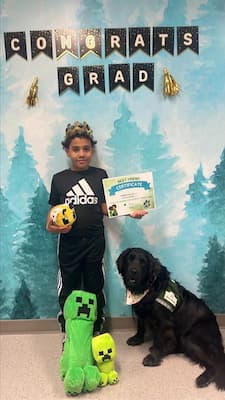 Lewis with CM facility dog, patsy. standing together under a congrats grad banner 