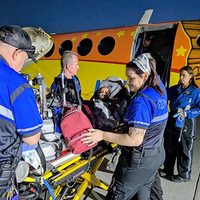 Medical transport team unloads infant Lilly in a car seat from an aircraft during a nighttime transfer to Children's Mercy.