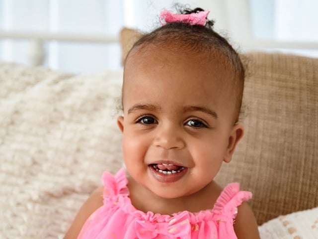 Close-up portrait of Lilly wearing a pink dress and pink hair bow while seated indoors.