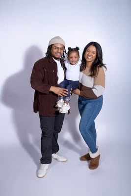 Dad James, Mom Taylor and baby Rose wearing brown toned clothing with white studio background.