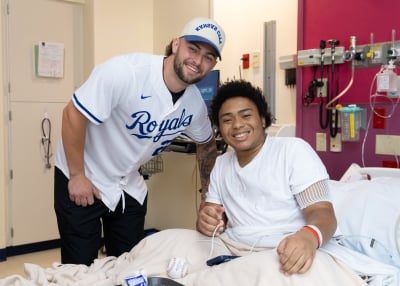 A patient in a hospital bed smiles as he gets a visit from Carter Jensen of the Kansas City Royals.