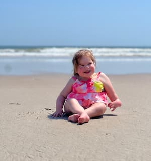 zyalee sitting in the sand on the beach with tie die swimsuit