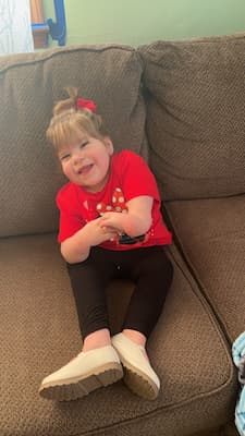 Zaylee sitting on the couch at home with a red shirt on