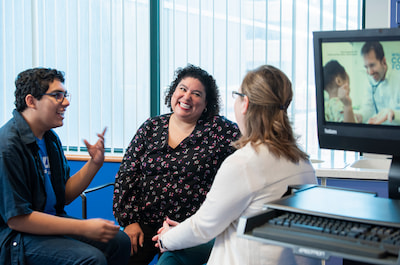 A male teenage patient and his parent talk with a health care provider in an exam room.