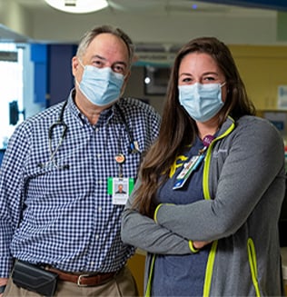 Shauna Becker, RN with Dr. Alan Gamis. They are wearing face masks and  standing inside Children's Mercy.