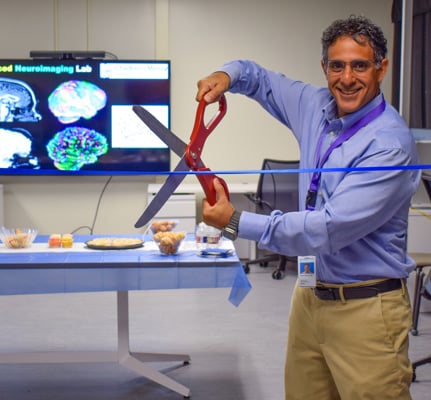 Dr. Avner Meoded uses large scissors to cut a ribbon at a grand opening ribbon cutting for his lab.