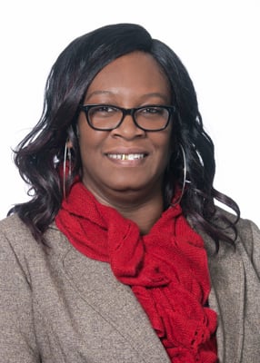 RJ Brooks. She has dark colored hair and is wearing glasses. She is wearing red scarf and a light brown jacket. 