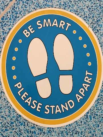 Floor sticker that reads "Be Smart Please Stand Apart"