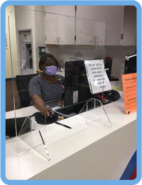 Staff member in face mask sitting behind desk and plexiglass wall