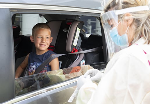 Nurse in PPE greeting boy in a car
