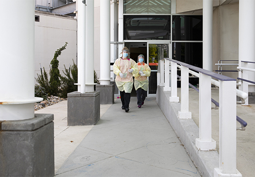 Two nurses in PPE walking from building