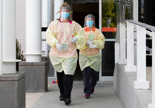 Two nurses in PPE walking from building