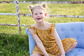 Quinn Liberman in a yellow sundress, sitting crossed-legged on a blue couch and smiling