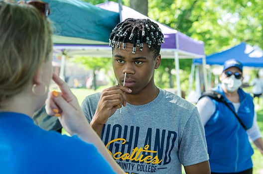 A Black teenage boy with braids inserts a nasal swab in his nostril.