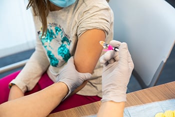 Two gloved hands administering a vaccination into a child's arm at Children's Mercy.