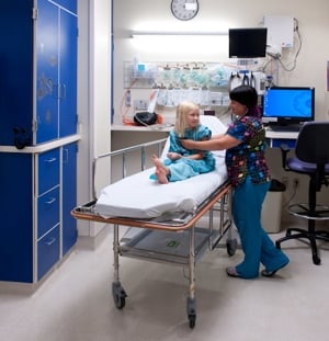 patient in hospital gown sitting on wheeled bed waiting with nurse before going to procedure/ operating room.