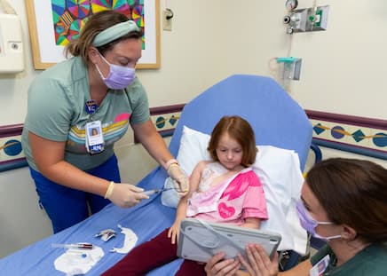 patient watching videos on a tablet while sitting on parents lap. All while port is being accessed.